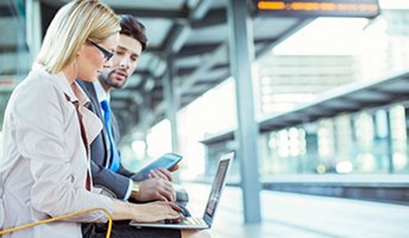 Man and Woman on laptops on a train station bench
